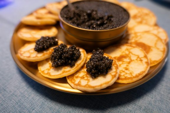 Ein Teller mit kleinen Pfannkuchen, garniert mit schwarzem Kaviar in einer Schale.