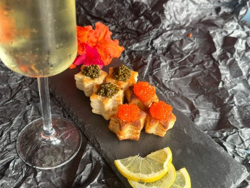 Lachsfilet-Häppchen mit Kaviar, Zitrone und Champagner, serviert auf schwarzem Stein.