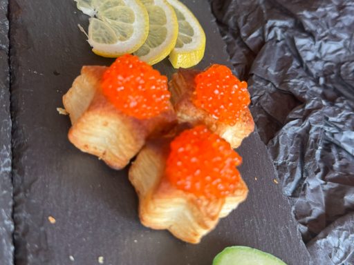 Drei quadratische Häppchen mit orangefarbenem Kaviar und Zitronenscheiben.