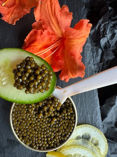 Gurke mit Kaviar und Zitronenscheiben, umgeben von roten Blüten.