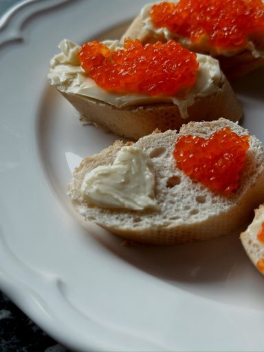 Zwei Brotscheiben mit Butter und rotem Kaviar, eine mit Herzform.